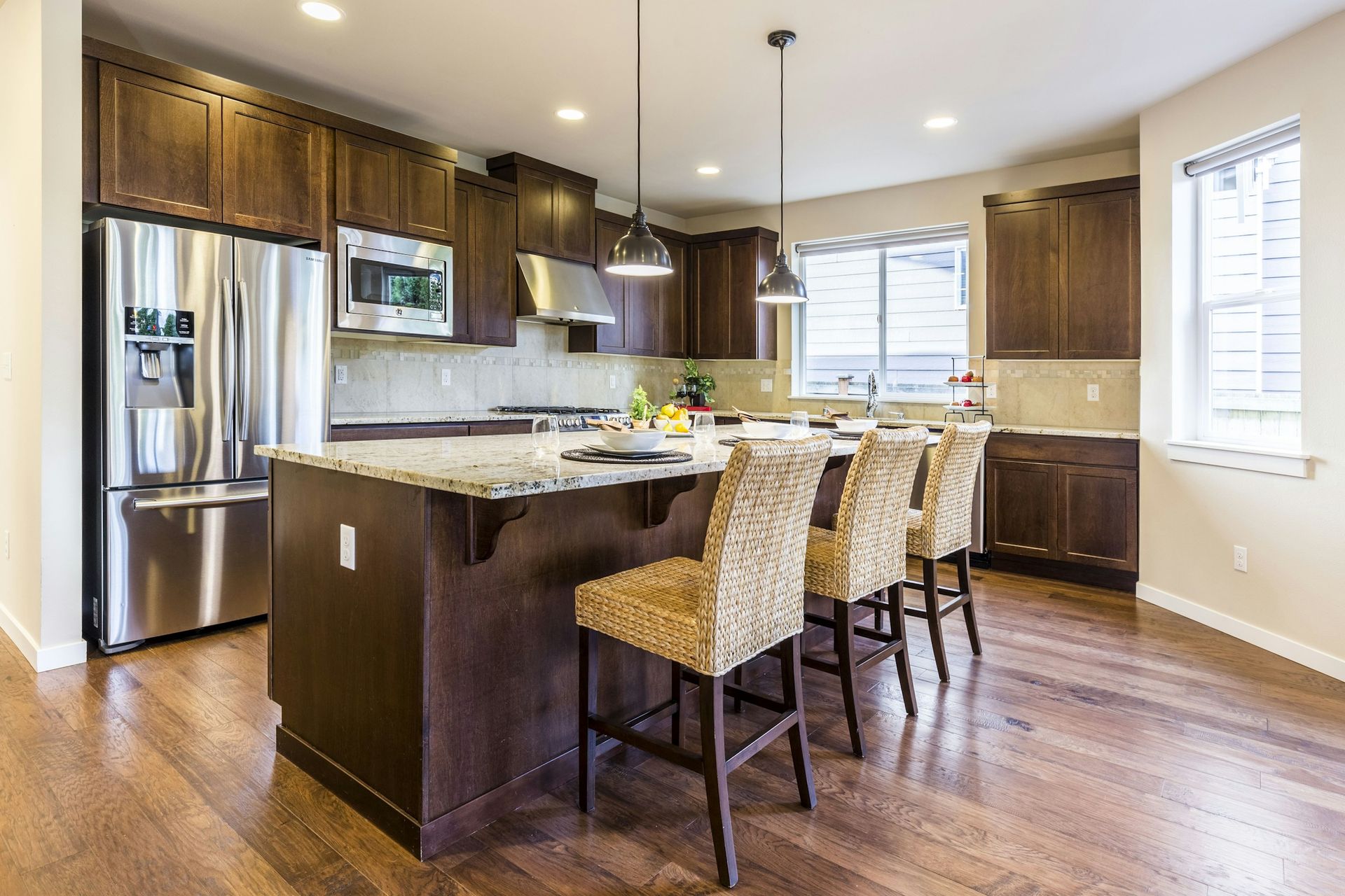 Kitchen island with a light speckled granite top, dark wood cabinets and woven bar stools