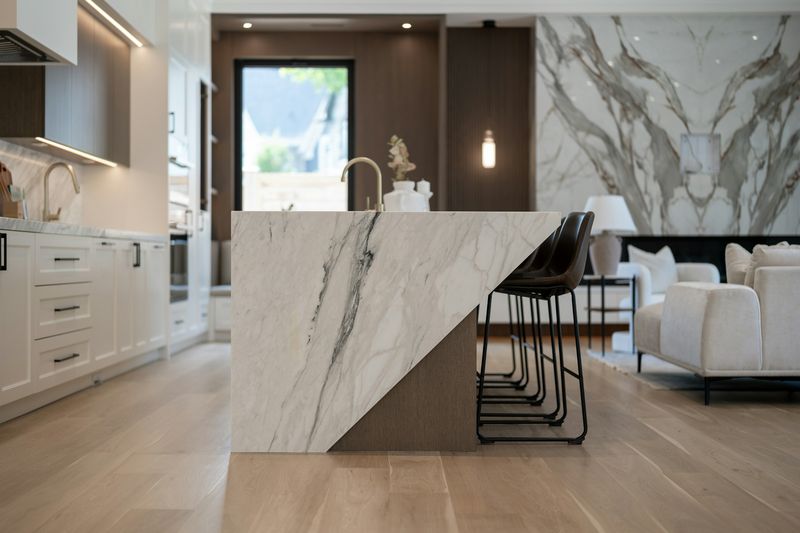Waterfall island in white stone with bold dark veining, bar stools alongside